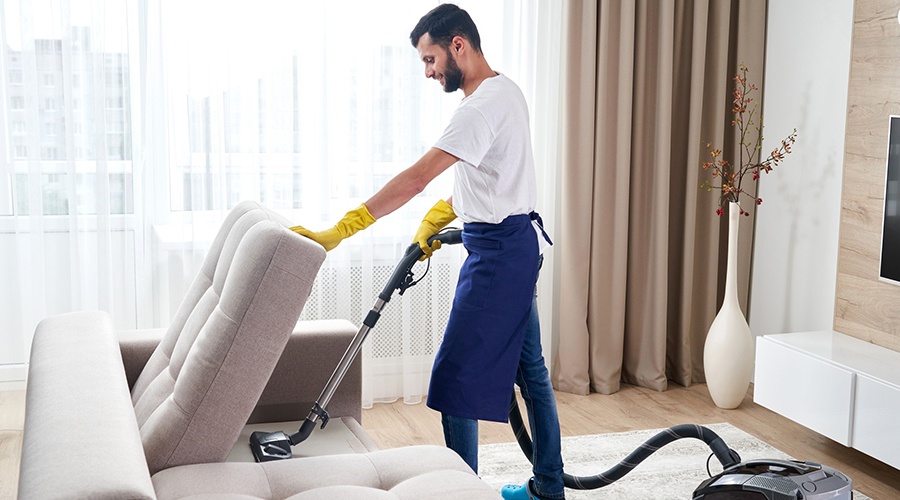 young-man-cleaning-sofa-with-vacuum-cleaner-leaving-room-home HCi